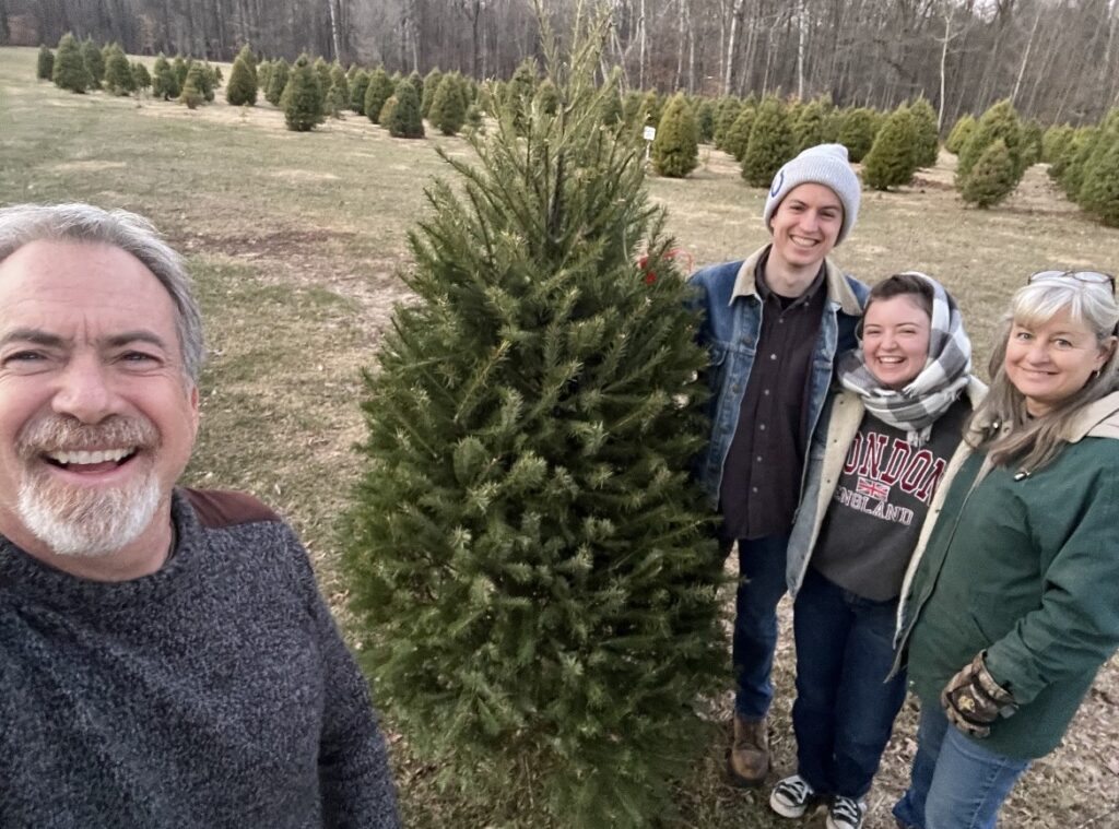 Family standing beside a Christmas tree at Hunter’s Honey Farm in Martinsville, Indiana, showing the local, family-owned Christmas tree farm tradition.